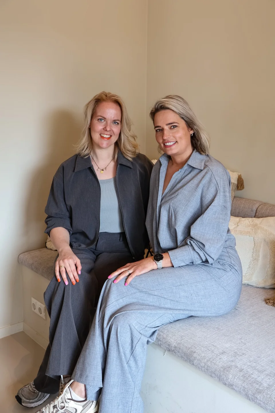 Anne en Daniëlle samen op de bank, in grijze en blauwe kleding